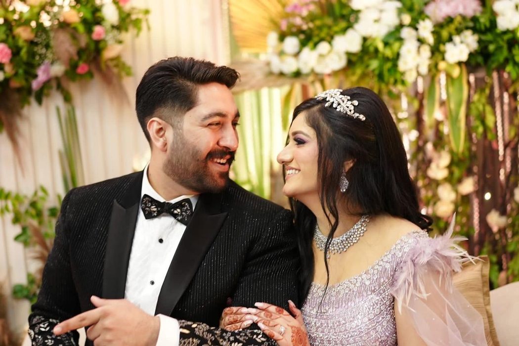 The couple laughing together in front of a wall of flowers.