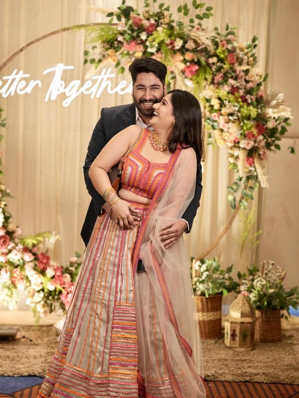 The couple laughing in front of a flower arch.